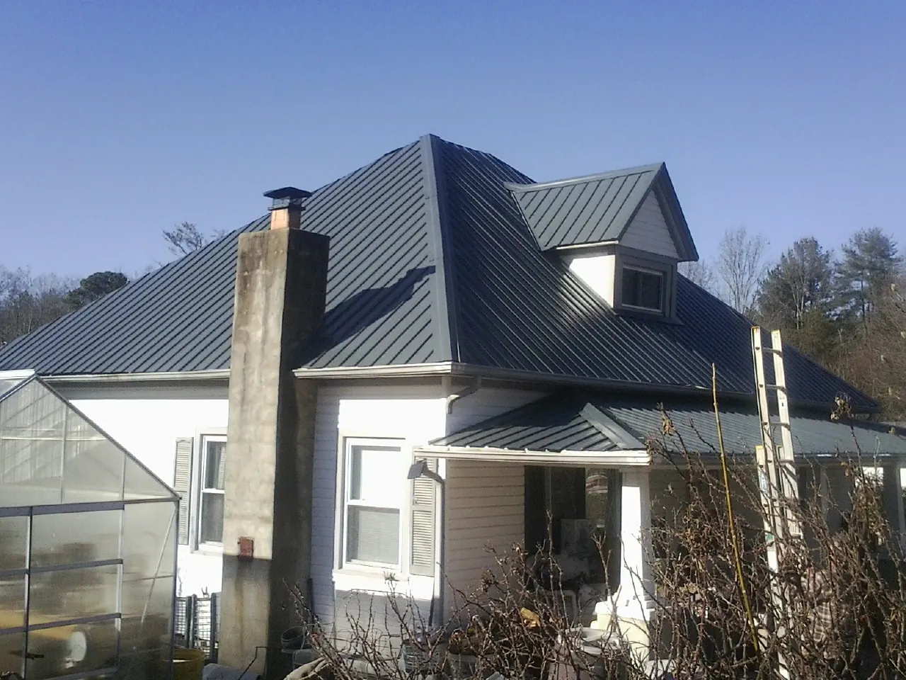 Dark blue standing seam metal roof on a white farmhouse with dormer — Slate & Tile Roof Repair by Roofing Brothers in Ottsville
