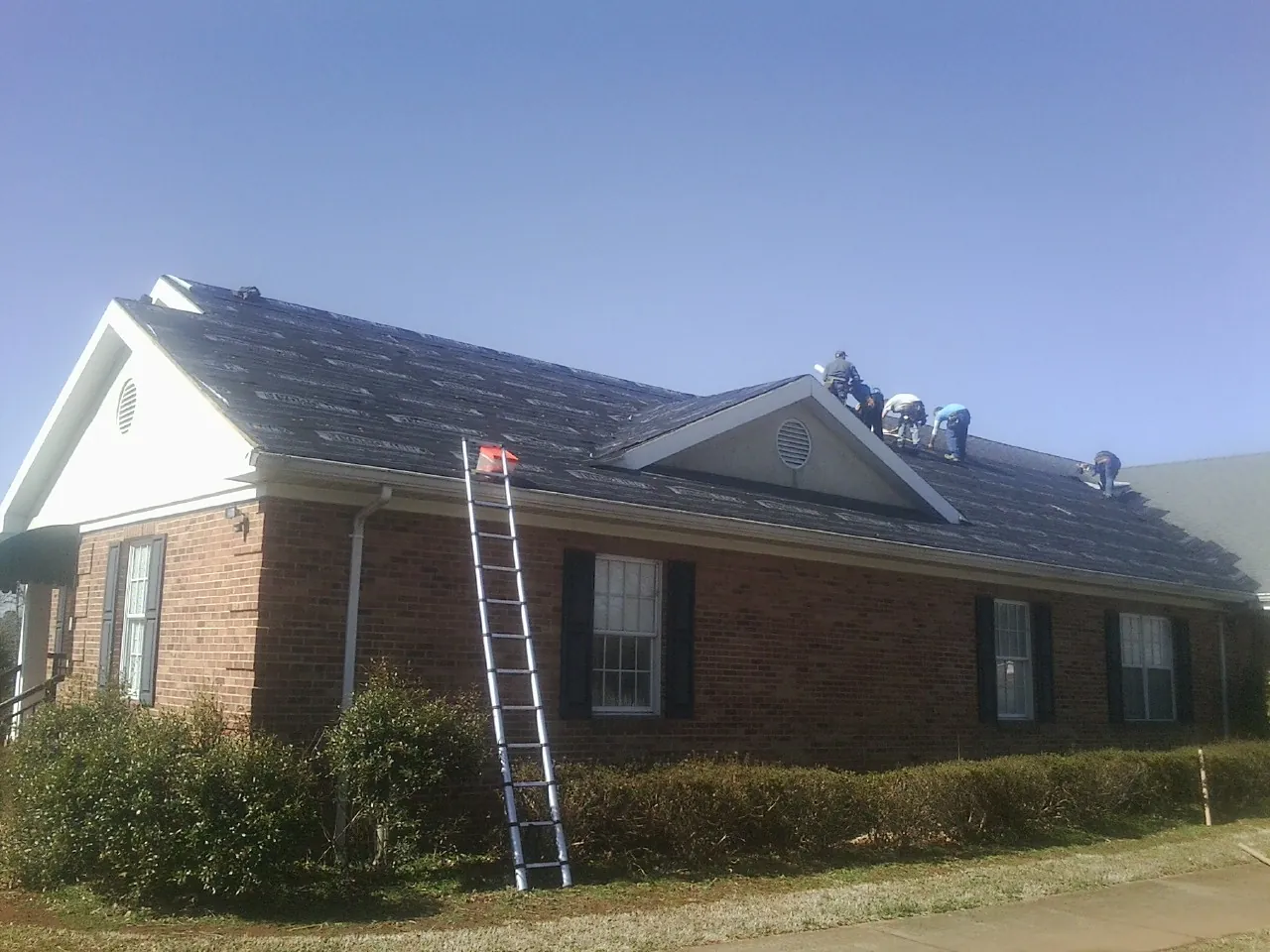 Crew tearing shingles off a brick ranch roof with a ladder set — Emergency Roof Repair work by our crew in Ottsville