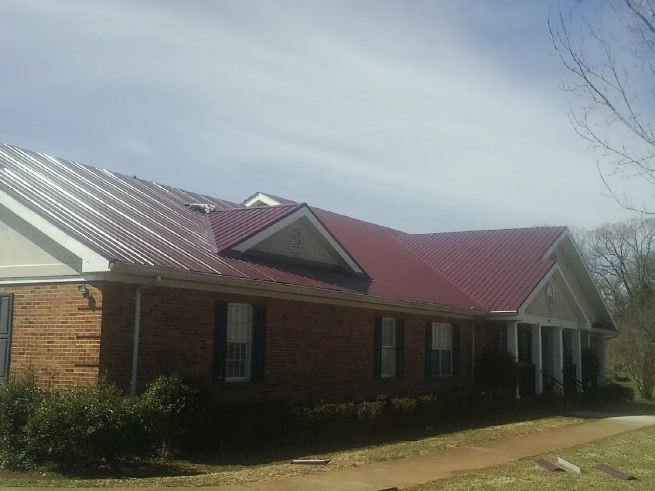 Red metal roof with gabled entries on a long brick building, from a Hail Damage Roof Repair job in Ottsville