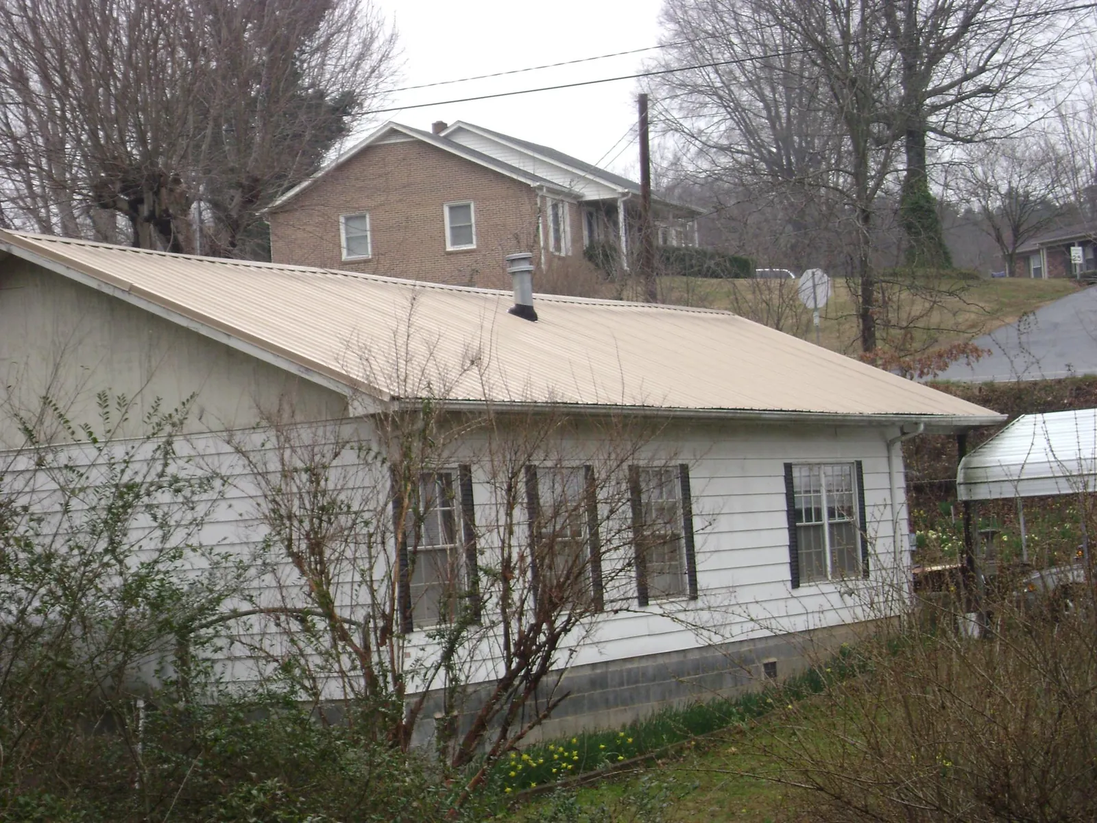 Tan metal roof on a white sided house set into a hillside — Commercial Roofing by Roofing Brothers in Ottsville